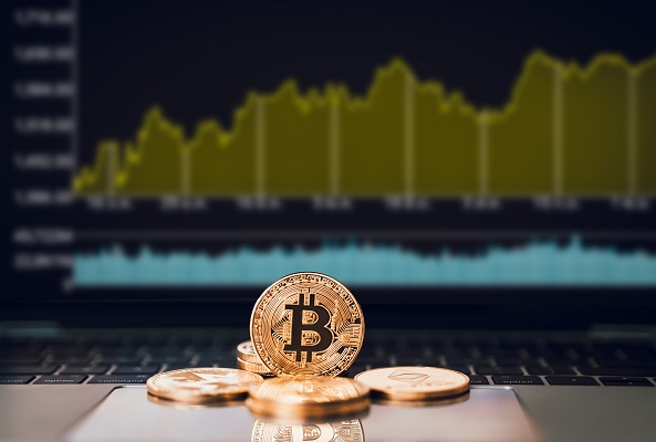 Foto: insígnias de bitcoins em frente ao computador