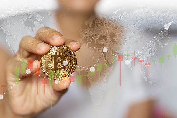 Foto: Mão segurando um bitcoin e detealhes de gráfico